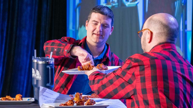 Mitch Teich offers Aaron Knight a chicken wing during the 2023 Association Update